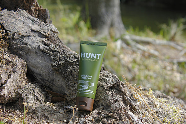 An image of a bottle of HUNT Repellent on the ground in font of a piece of wood. There is a river in the background.