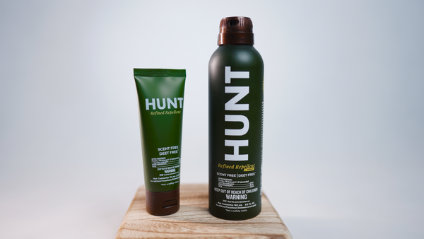 HUNT Refined Repellent Lotion and Spray on a wooden block with a white background.