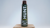 Hunt Refined Repellent Spray bottle on a wooden block with a gray background.