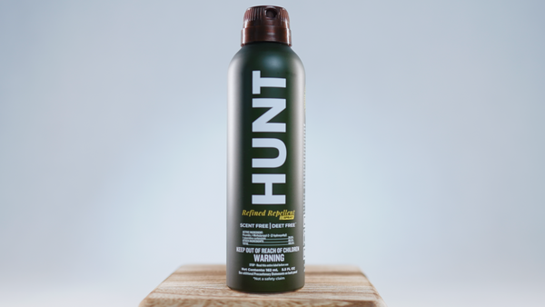 Hunt Refined Repellent Spray bottle on a wooden block with a gray background.