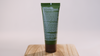 Green tube of Hunt Refined Repellent Lotion on a wooden block with a white background. It is facing backwards to show to information on the back of the bottle.